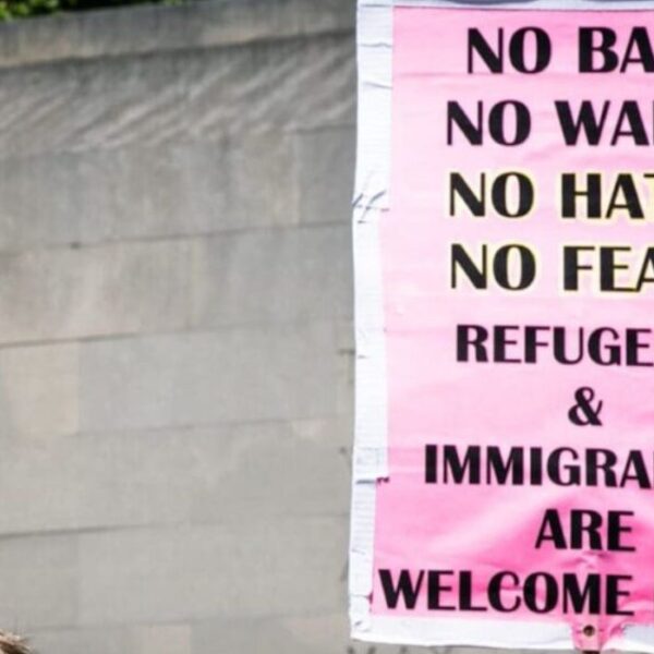 Un cartello rosa con scritta nera dice "No ban, no wall, no hate, no fear. Refugees and mkgrants are welcome here.
